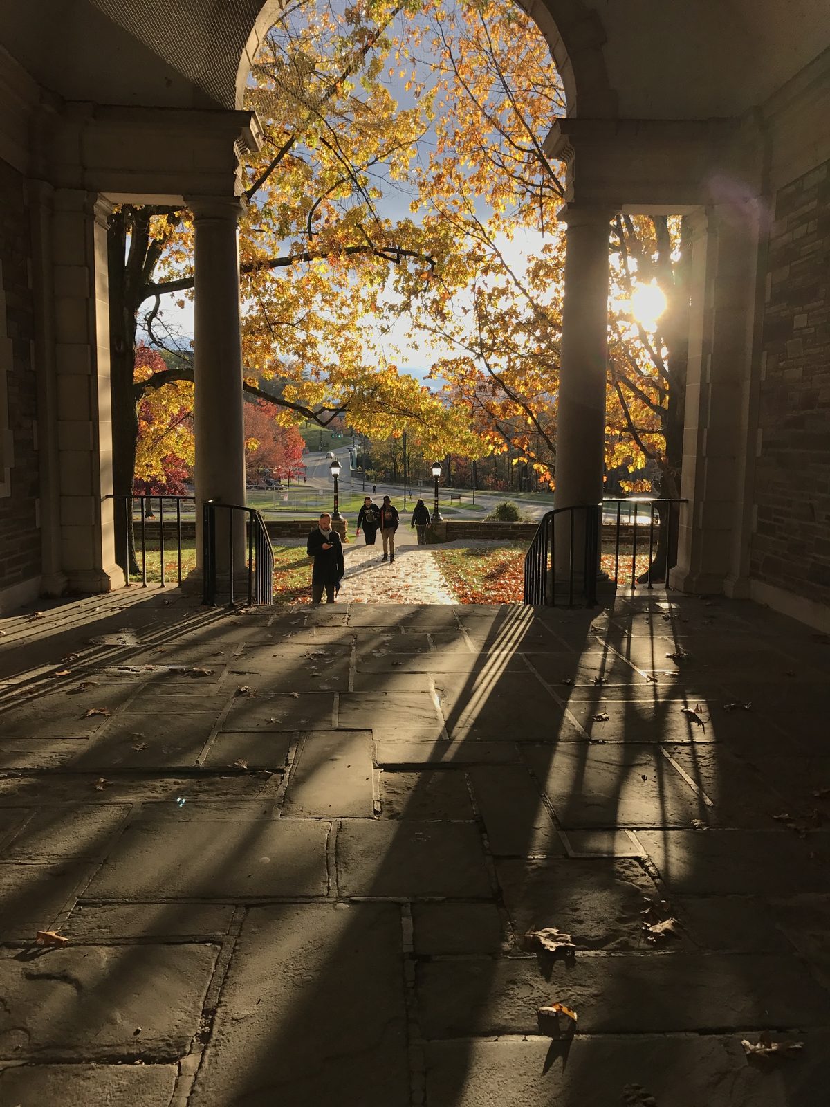 Students walking down stone steps under an archway on the Cornell campus in autumn.